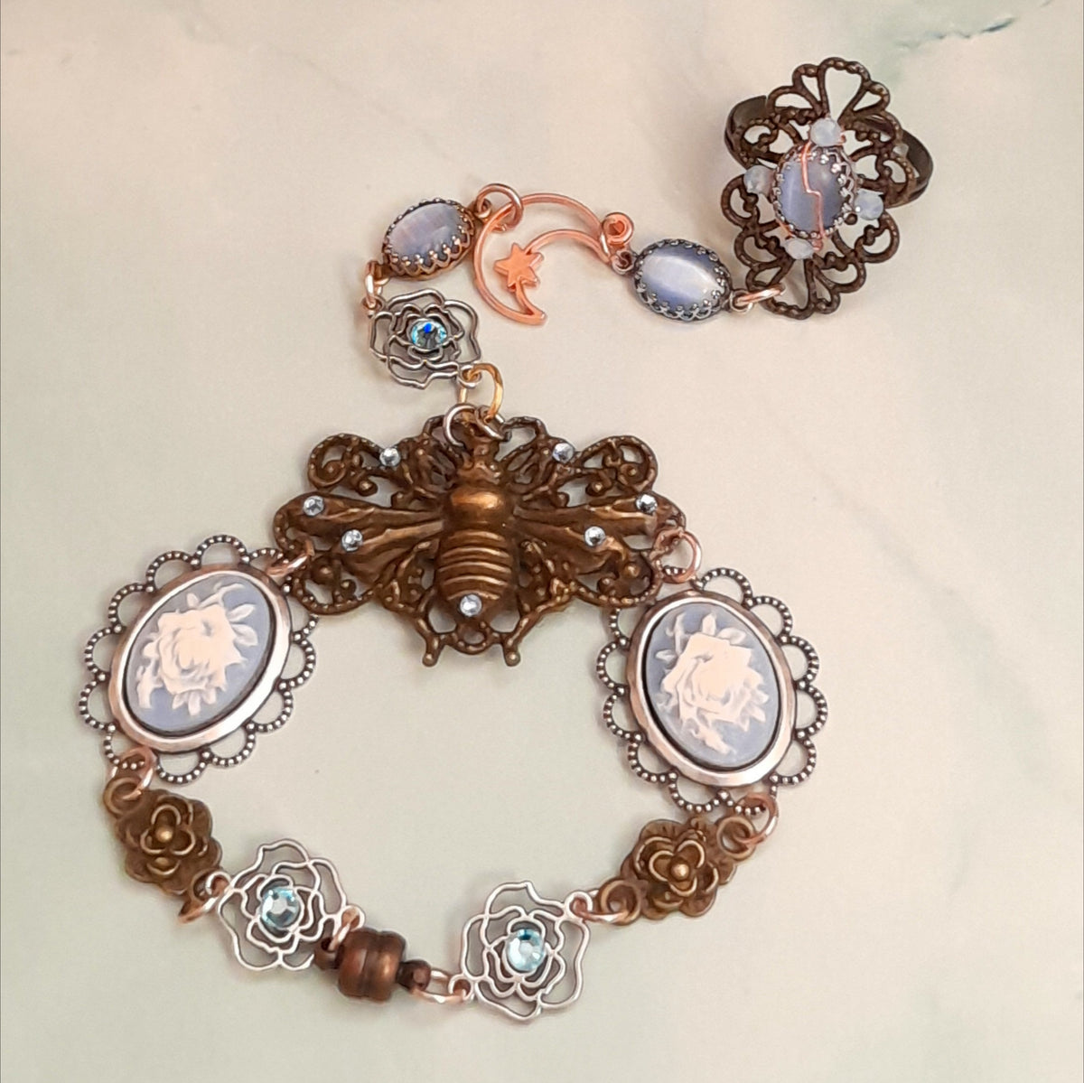 Magical fantasy bee hand chain slave bracelet worn on hand top down view showing full piece from filigree ring to bee centerpiece with blue Swarovski crystals Victorian style vintage style