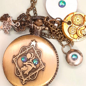 Alice in Wonderland pocket watch necklace back view showing Cheshire Cat engraving with steampunk gear and crystal disc charms antiqued brass Victorian style vintage style fantasy handmade swarovski crystals