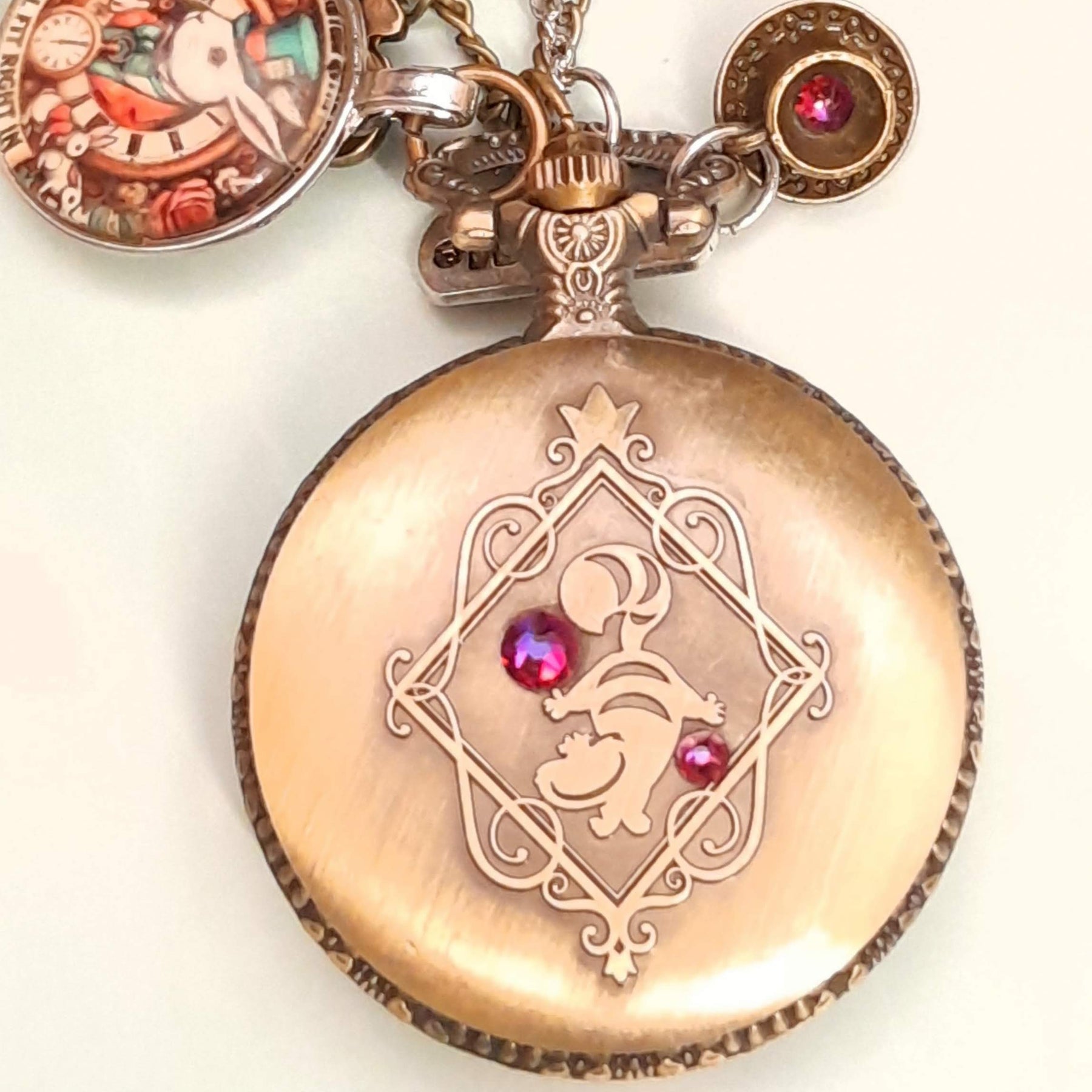 Alice in Wonderland pocket watch necklace held in hand showing front engraved design with red Swarovski crystals antiqued brass Victorian style vintage style fantasy handmade