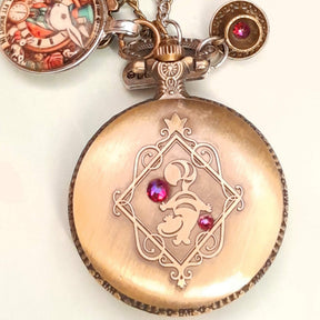 Alice in Wonderland pocket watch necklace held in hand showing front engraved design with red Swarovski crystals antiqued brass Victorian style vintage style fantasy handmade