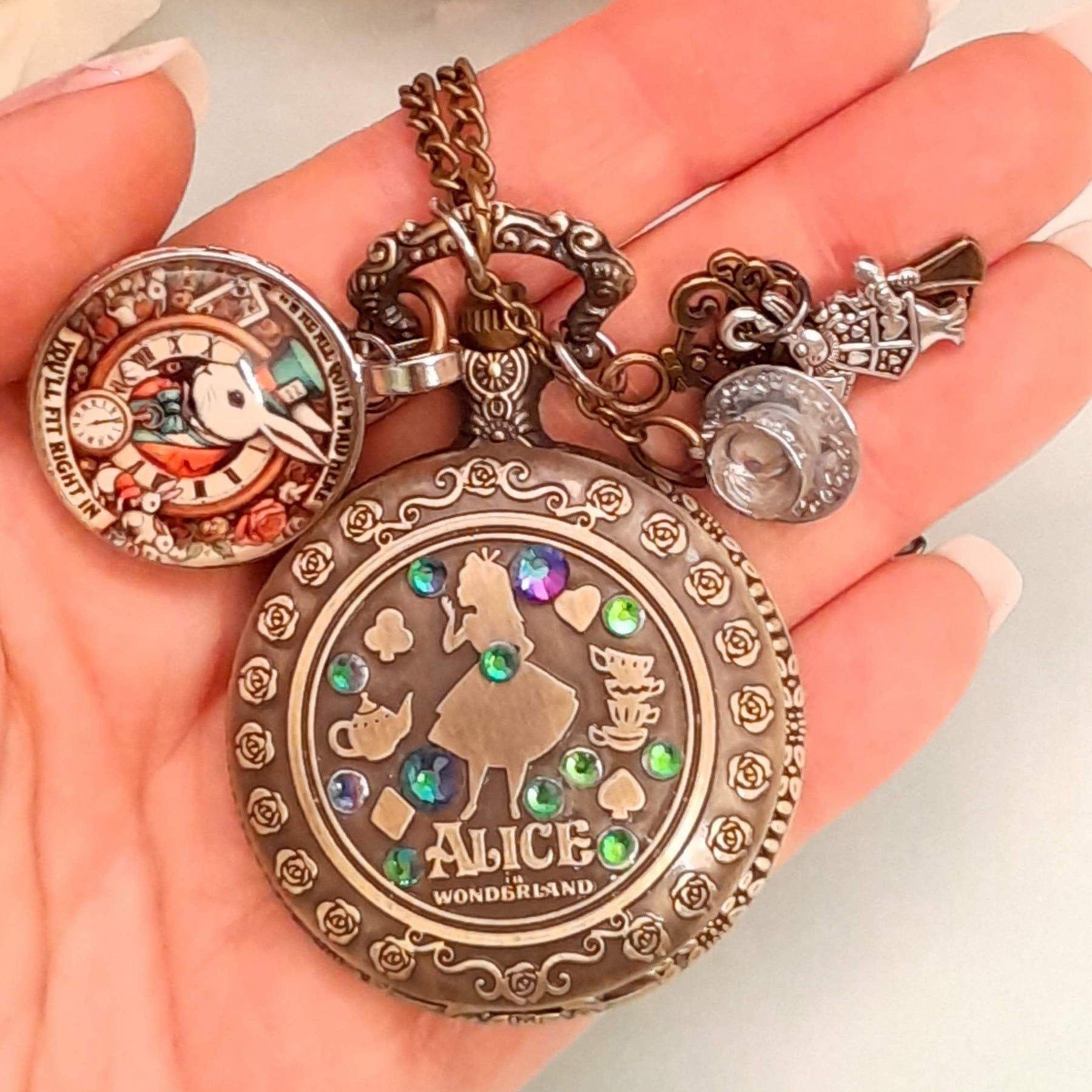 Alice in Wonderland pocket watch necklace held in hand showing Alice silhouette with multicolor Swarovski crystals White Rabbit and teacup charms antiqued brass Victorian style vintage style fantasy handmade