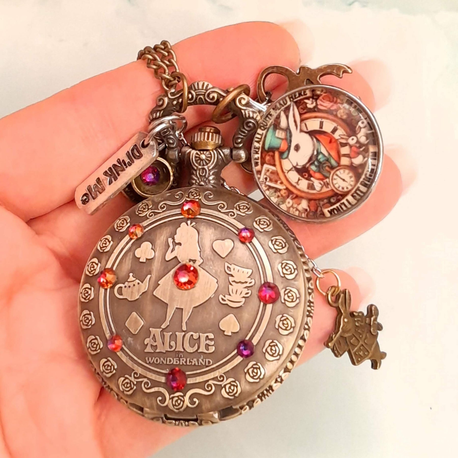 Alice in Wonderland pocket watch necklace held in hand full front view with White Rabbit charm and red Swarovski crystals antiqued brass Victorian style vintage style fantasy handmade