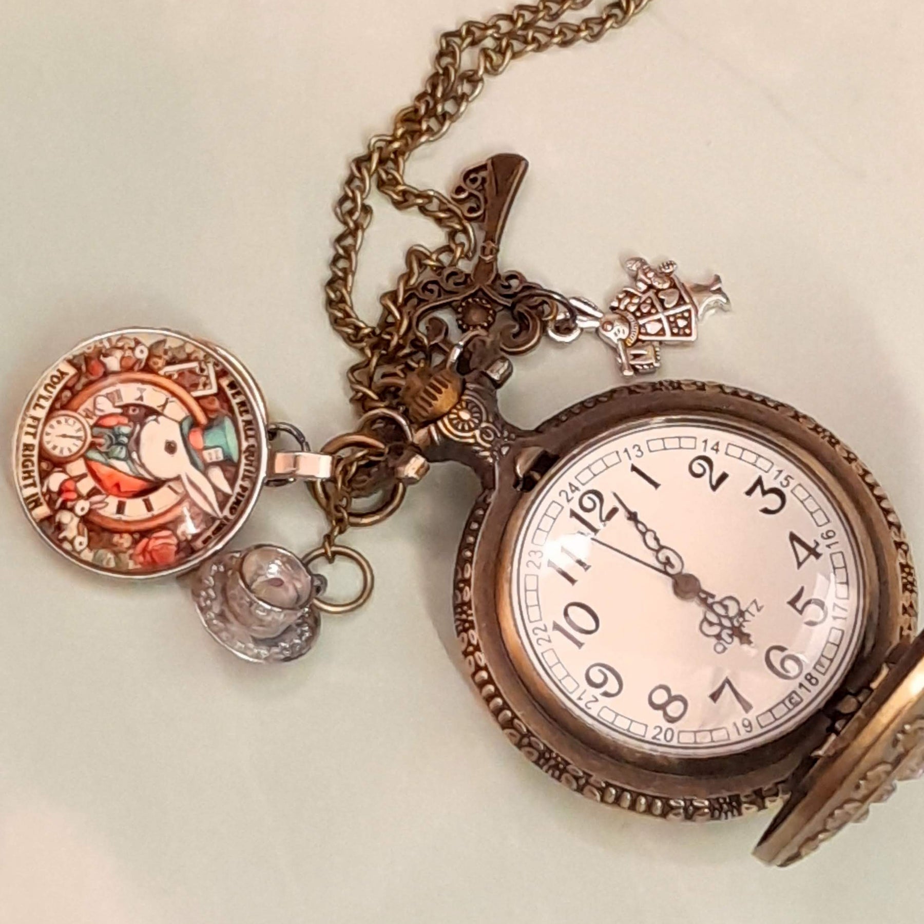 Alice in Wonderland pocket watch necklace open showing working clock face with White Rabbit and teacup charms antiqued brass Victorian style vintage style fantasy handmade swarovski crystals
