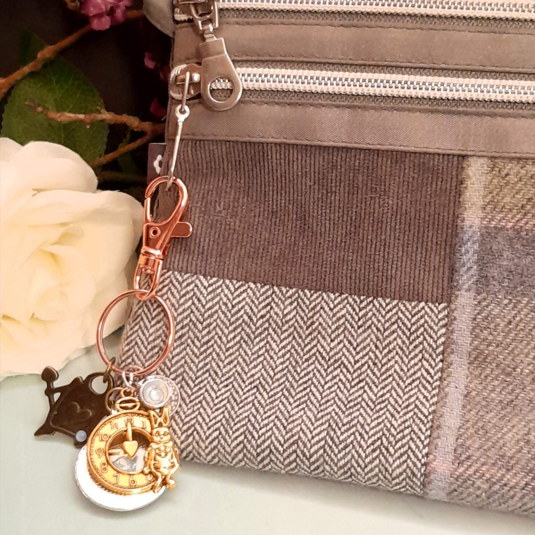 Side view of magical fantasy Alice in Wonderland purse charm clipped to tan herringbone bag with clock face, White Rabbit figurine and Swarovski crystal teacup charm, Victorian style vintage style
