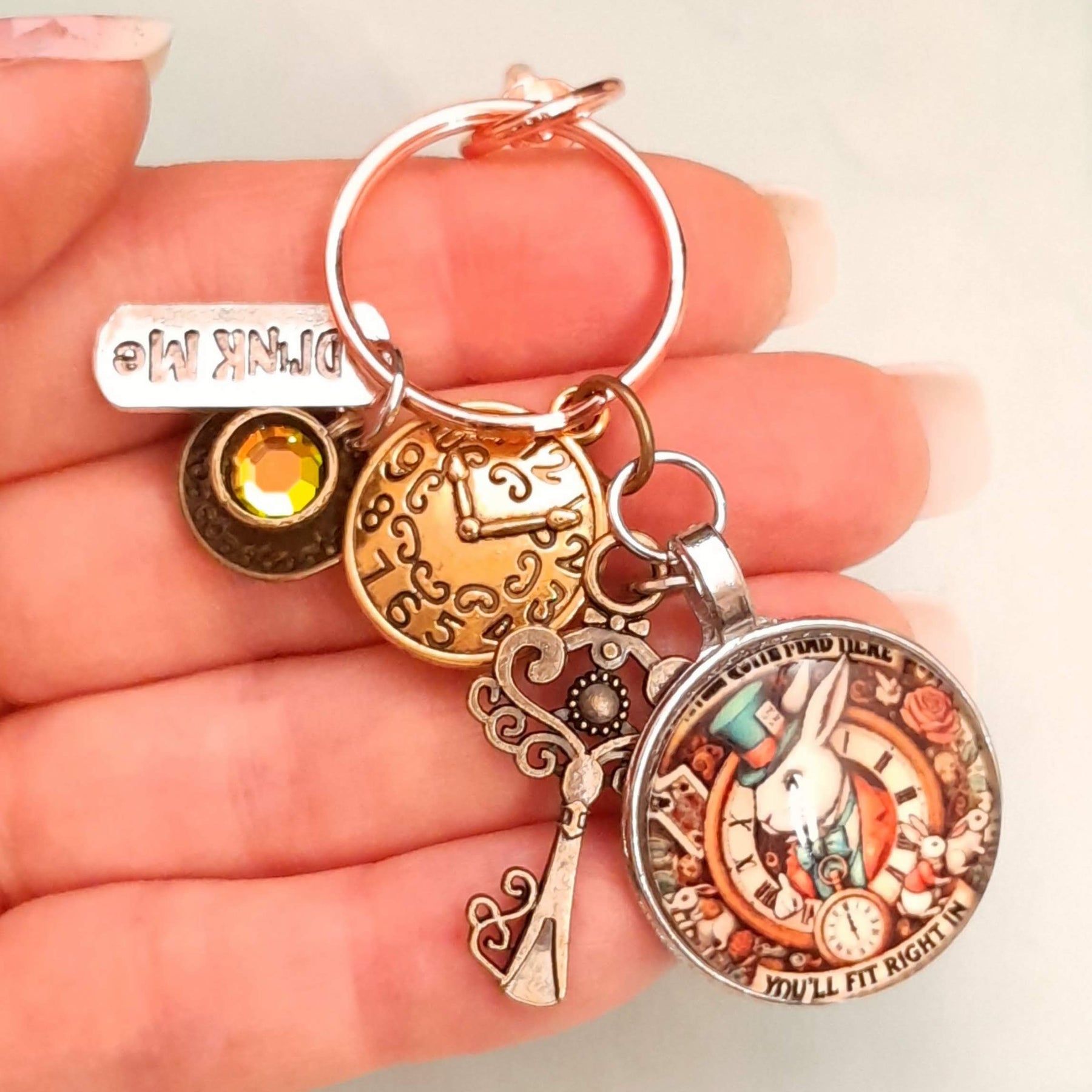 Alice in Wonderland magical fantasy purse charm held in hand showing White Rabbit clock face, Drink Me tag, clock charm, ornate key, and Swarovski crystal — Victorian style vintage style