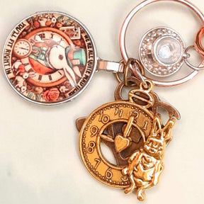 Flat lay detail of handmade magical fantasy Alice in Wonderland purse charm showing White Rabbit clock medallion, clock face charm, White Rabbit charm and Swarovski crystal teacup, Victorian style vintage style