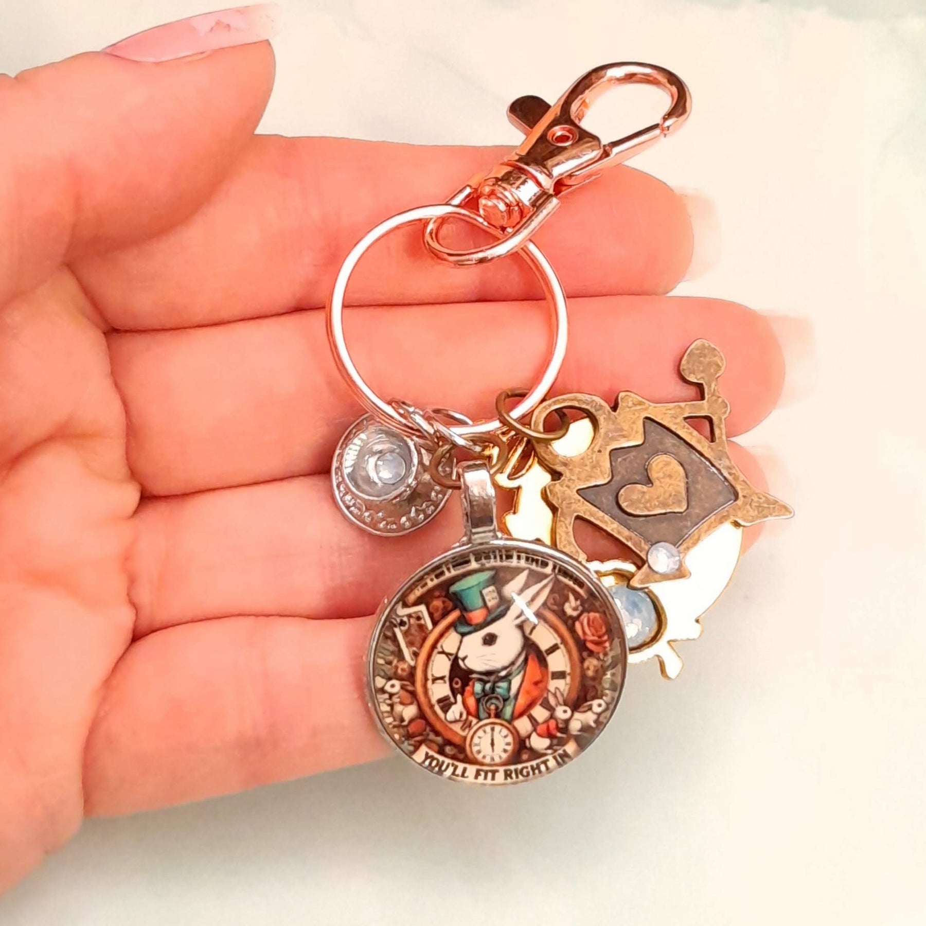 Handmade magical fantasy Alice in Wonderland purse charm held in hand showing White Rabbit clock medallion, Queen of Hearts and Swarovski crystal teacup charm, Victorian style vintage style