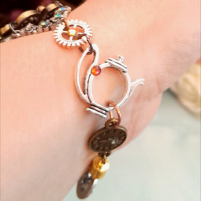 Handmade Alice in Wonderland Victorian style hand chain watch close up of adjustable ring with steampunk gear teapot charm and Roman numeral clock disc with Swarovski crystals