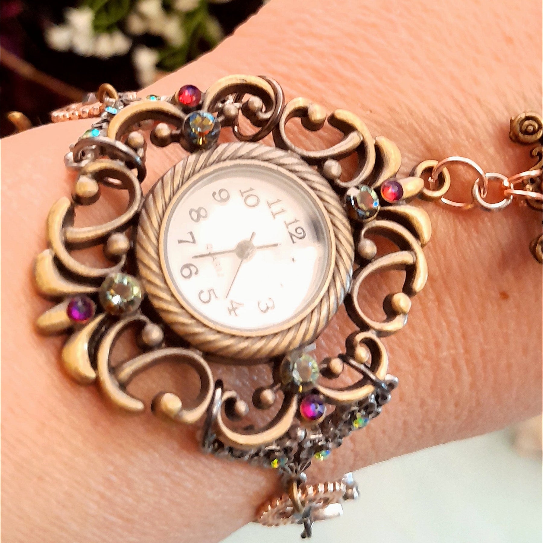 Alice in Wonderland Victorian style hand chain watch flat lay showing filigree watch face steampunk gear teapot charm and Roman numeral clock disc with Swarovski crystals