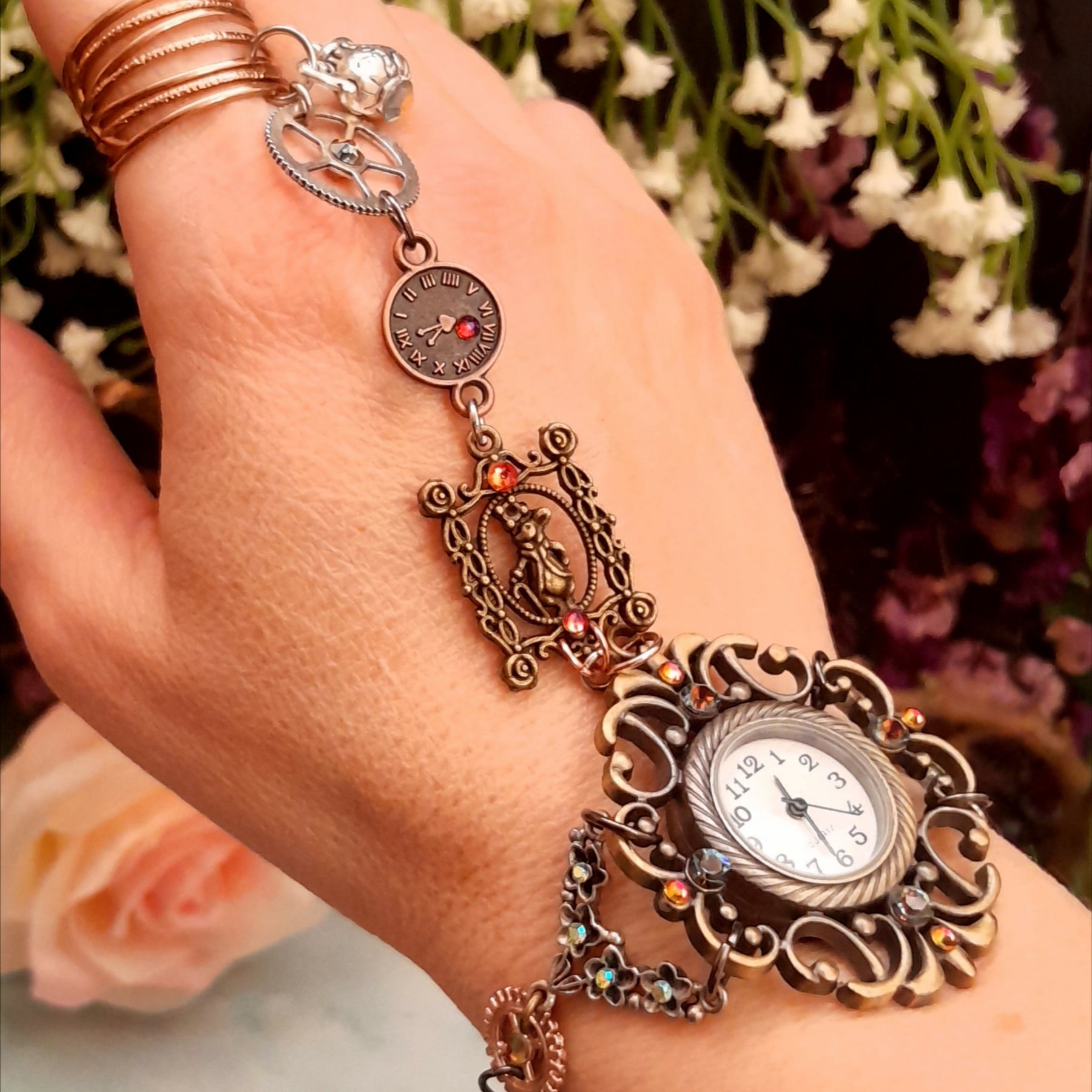 Handmade Alice in Wonderland Victorian style hand chain watch worn on hand showing full piece from ring to watch with Swarovski crystals and floral background