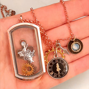 Magical fantasy Alice in Wonderland locket necklace close up showing White Rabbit inside locket, clock face, gear and teacup charms on chain, Victorian style vintage style