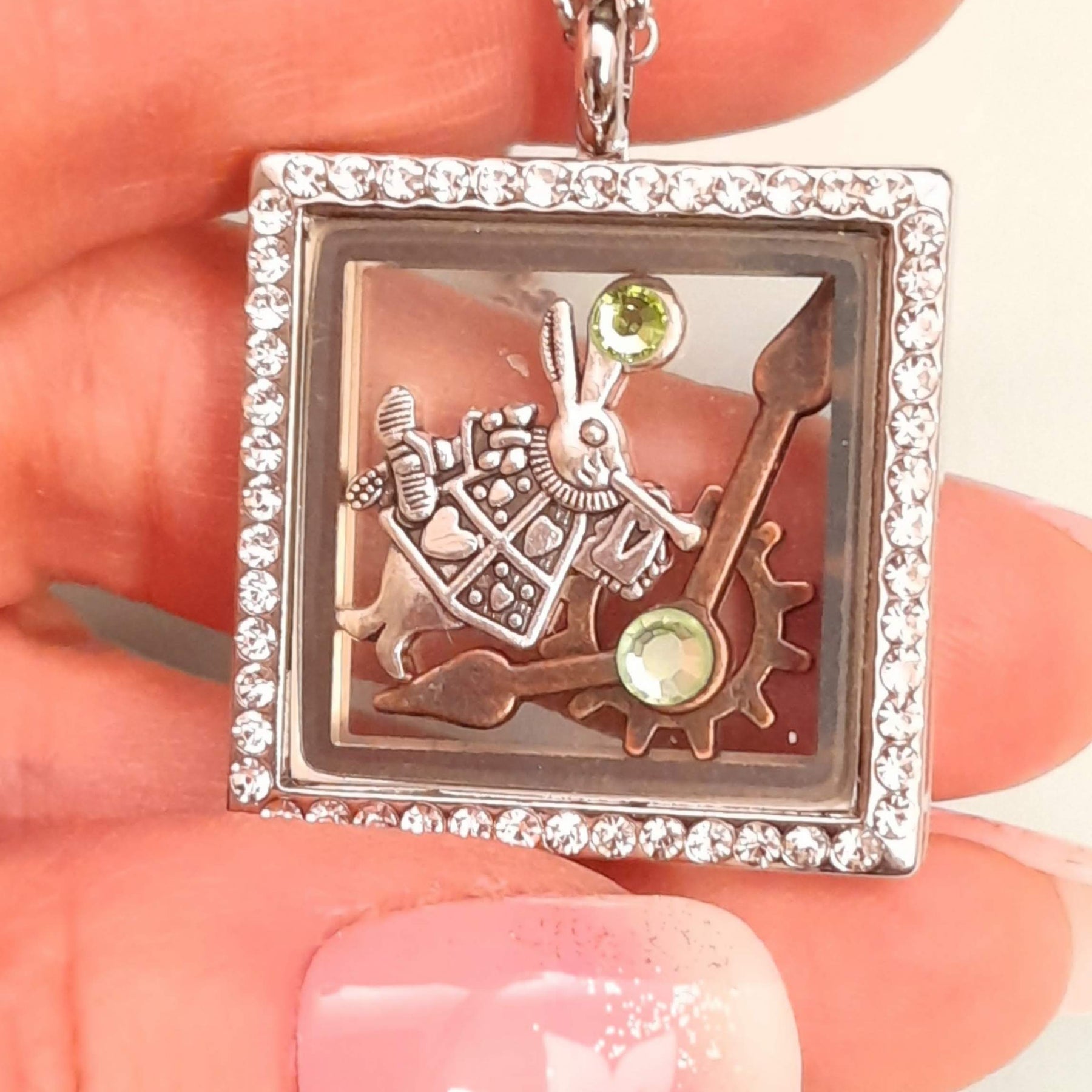 Handmade magical fantasy Alice in Wonderland square locket necklace held in hand showing full Swarovski crystal border, White Rabbit and clock hand charms inside, green crystal accents, Victorian style vintage style