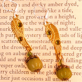 Victorian style vintage style handmade angel wing pumpkin earrings with Swarovski Olivine crystals displayed on an open book, magical fantasy jewelry by Rachel Flam Design