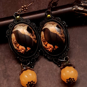 One-of-a-kind witchy earrings with black crows, warm autumn imagery, yellow Swarovski crystals, and dangling pumpkin details, Victorian style and vintage style magical fantasy jewelry by Rachel Flam Design