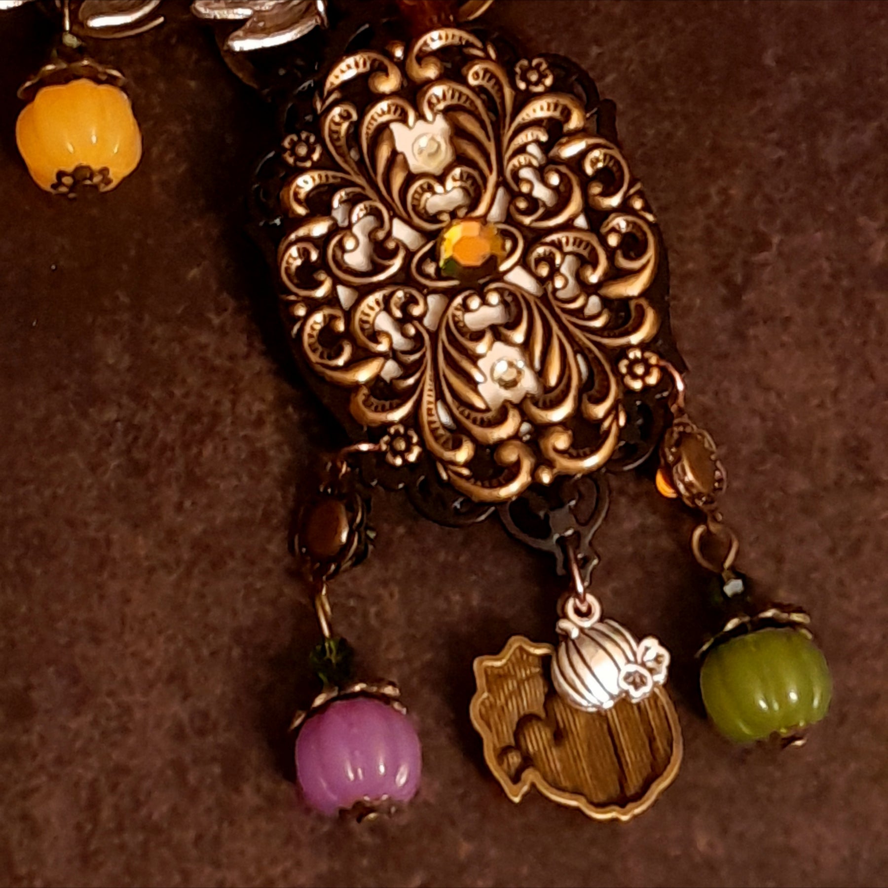 Back view of handmade black crow necklace showing the ornate filigree reverse, decorative crystal detail, leafy branches, pumpkins, and autumn dangles, Victorian style and vintage style fantasy jewelry by Rachel Flam Design