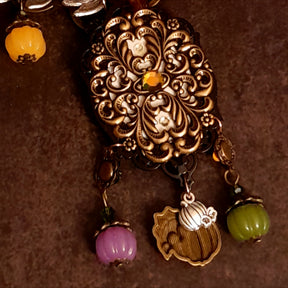 Back view of handmade black crow necklace showing the ornate filigree reverse, decorative crystal detail, leafy branches, pumpkins, and autumn dangles, Victorian style and vintage style fantasy jewelry by Rachel Flam Design