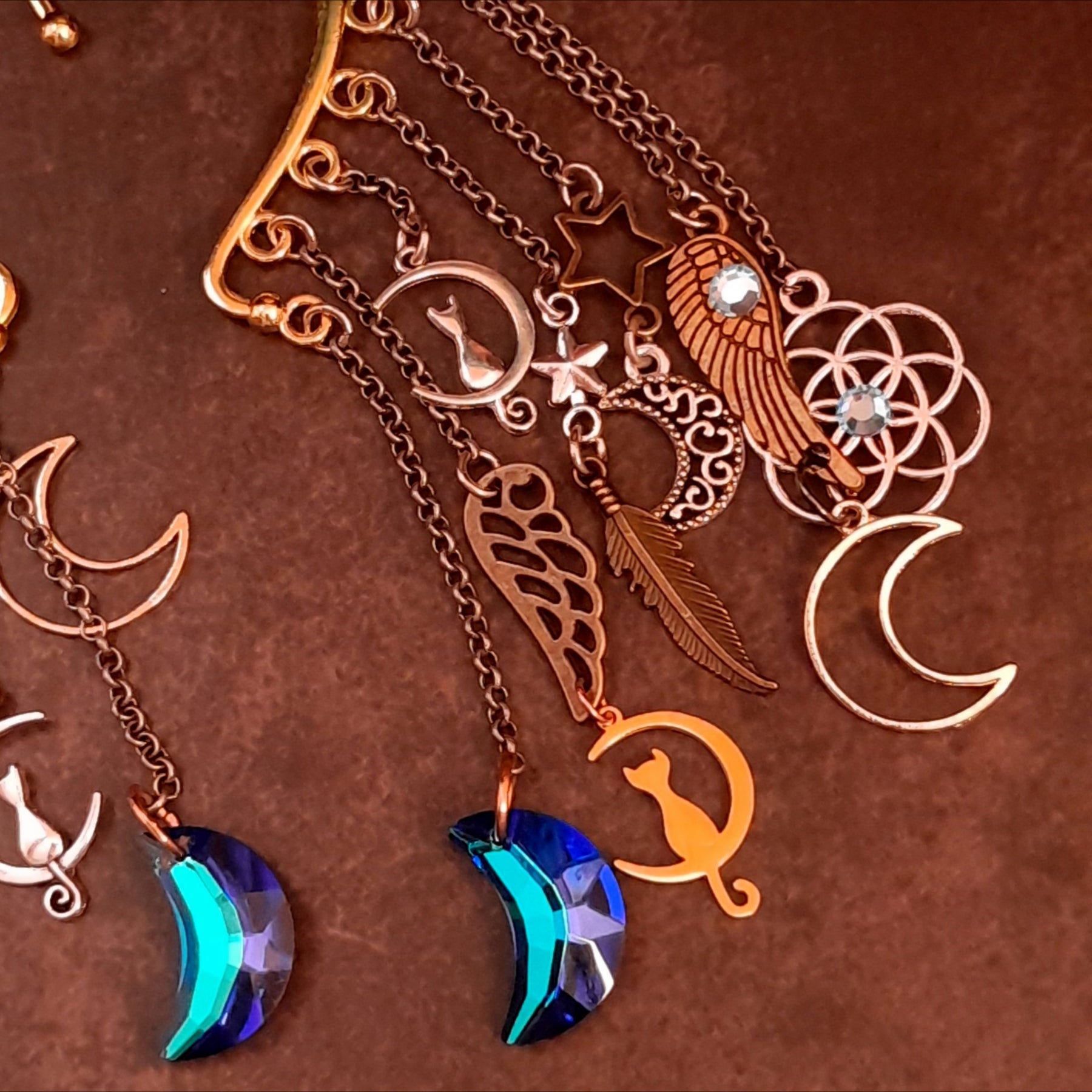 Detailed view of a Victorian style and vintage style celestial ear cuff by Rachel Flam Design, with Swarovski crystals, a blue crescent drop, cats, stars, wings and interlocking circular charms.