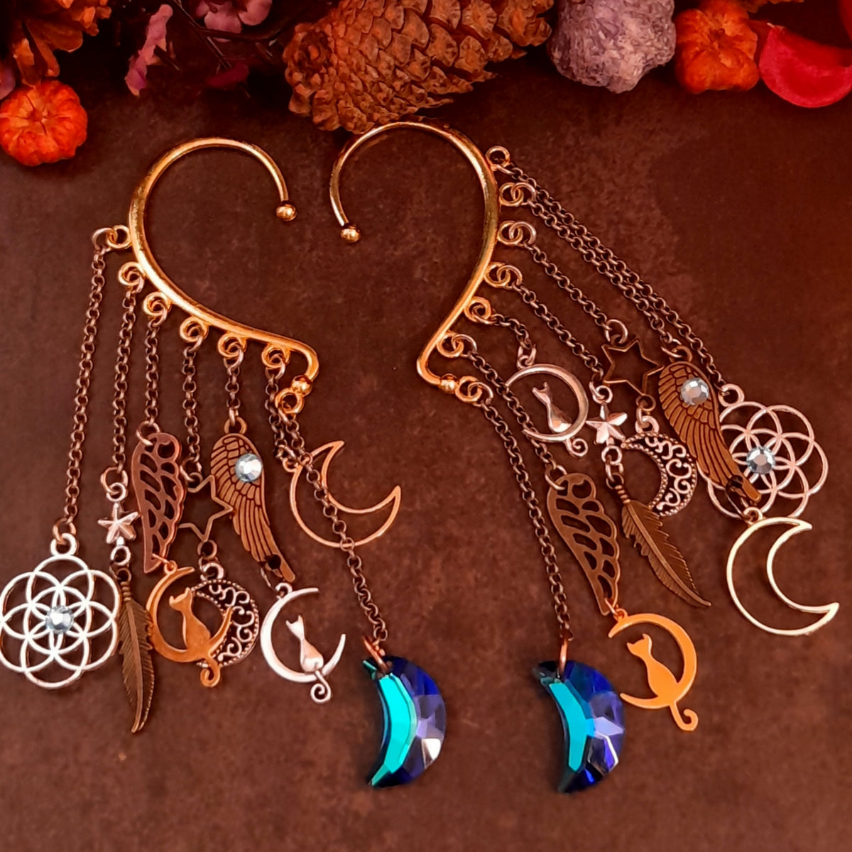 Handmade Victorian style and vintage style celestial ear wraps by Rachel Flam Design, with blue moon drops, cat charms, stars, wings and Swarovski crystals on a dark background.