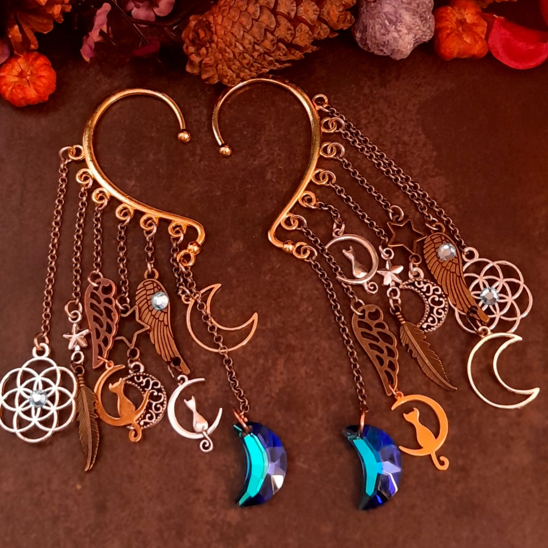 Handmade Victorian style and vintage style celestial ear wraps by Rachel Flam Design, with blue moon drops, cat charms, stars, wings and Swarovski crystals on a dark background.