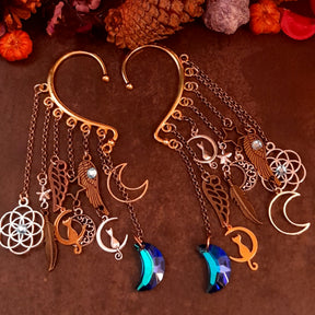 Handmade Victorian style and vintage style celestial ear wraps by Rachel Flam Design, with blue moon drops, cat charms, stars, wings and Swarovski crystals on a dark background.