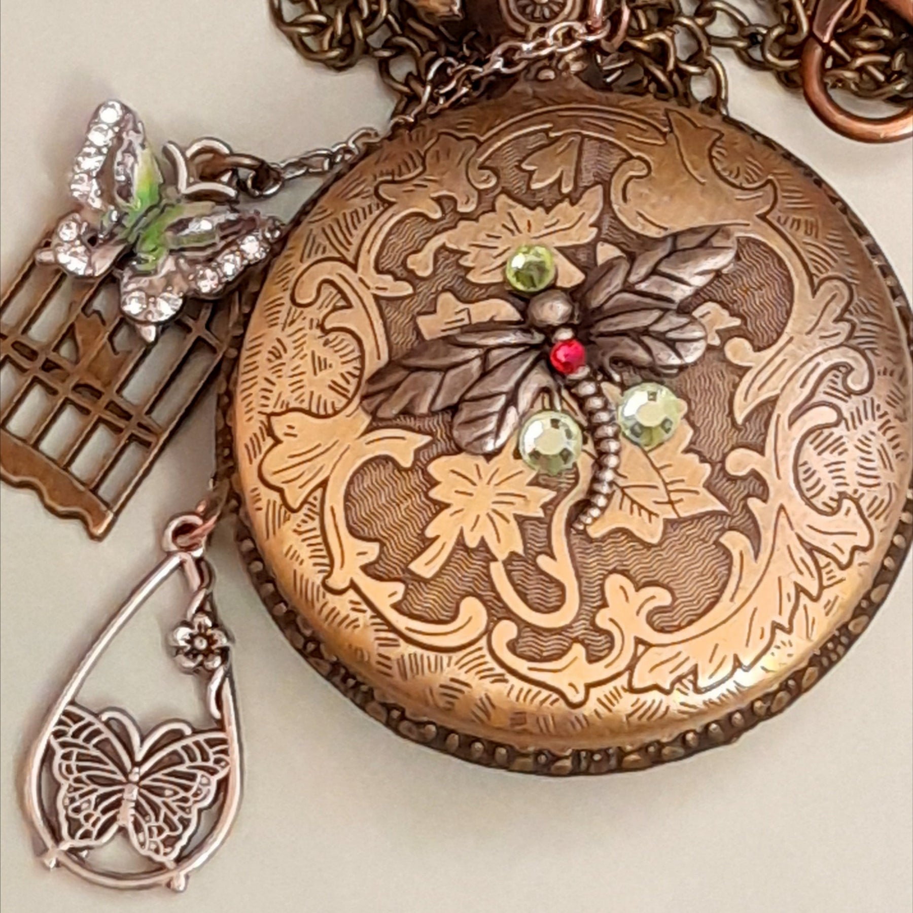 Handmade magical fantasy butterfly dragonfly pocketwatch necklace back close up with floral engraved antiqued brass, Swarovski crystals, enameled butterfly and birdcage charms, Victorian style vintage style