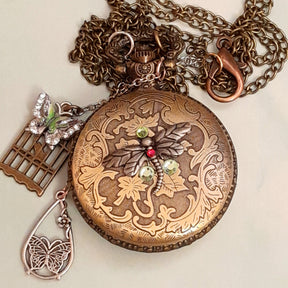 Handmade magical fantasy butterfly dragonfly pocketwatch necklace back view with floral engraved antiqued brass, Swarovski crystals, enameled butterfly and birdcage charms, Victorian style vintage style