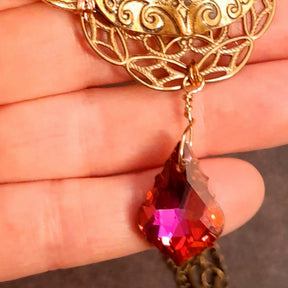 Close up of a Victorian style vintage style sparkling red and pink Swarovski crystal briolette drop dangling from a masquerade mask necklace pendant held in hand