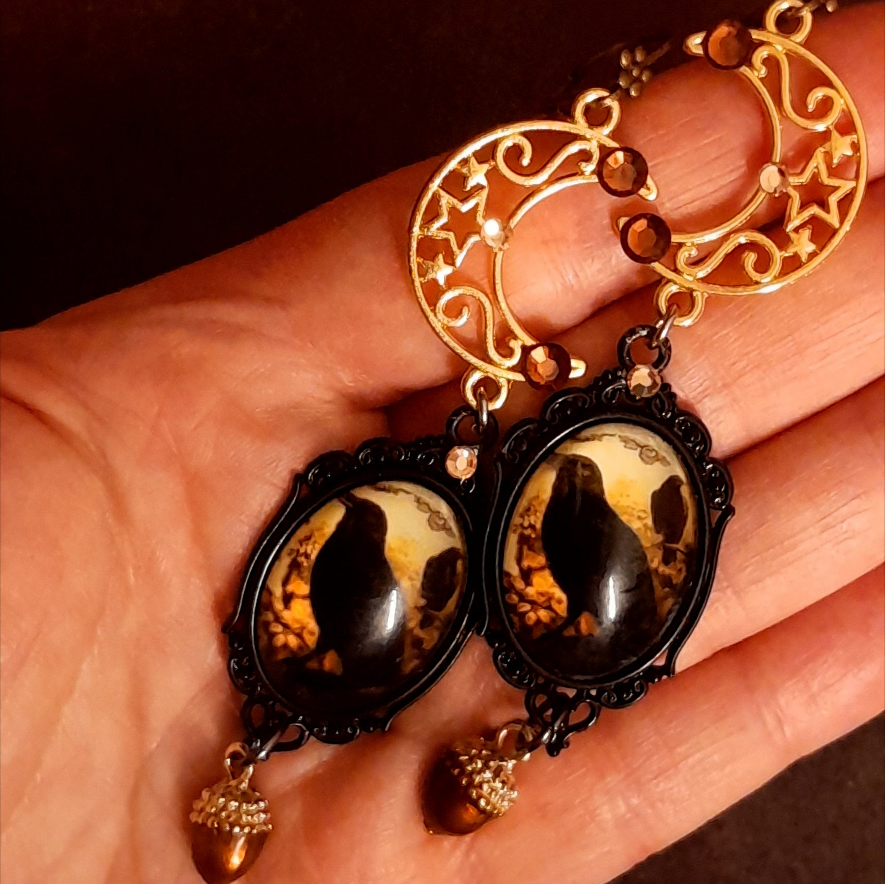 Long crow and crescent moon dangle earrings held in hand for scale with Swarovski crystals and acorn charms, Victorian style vintage style nature Halloween earrings, Rachel Flam Design