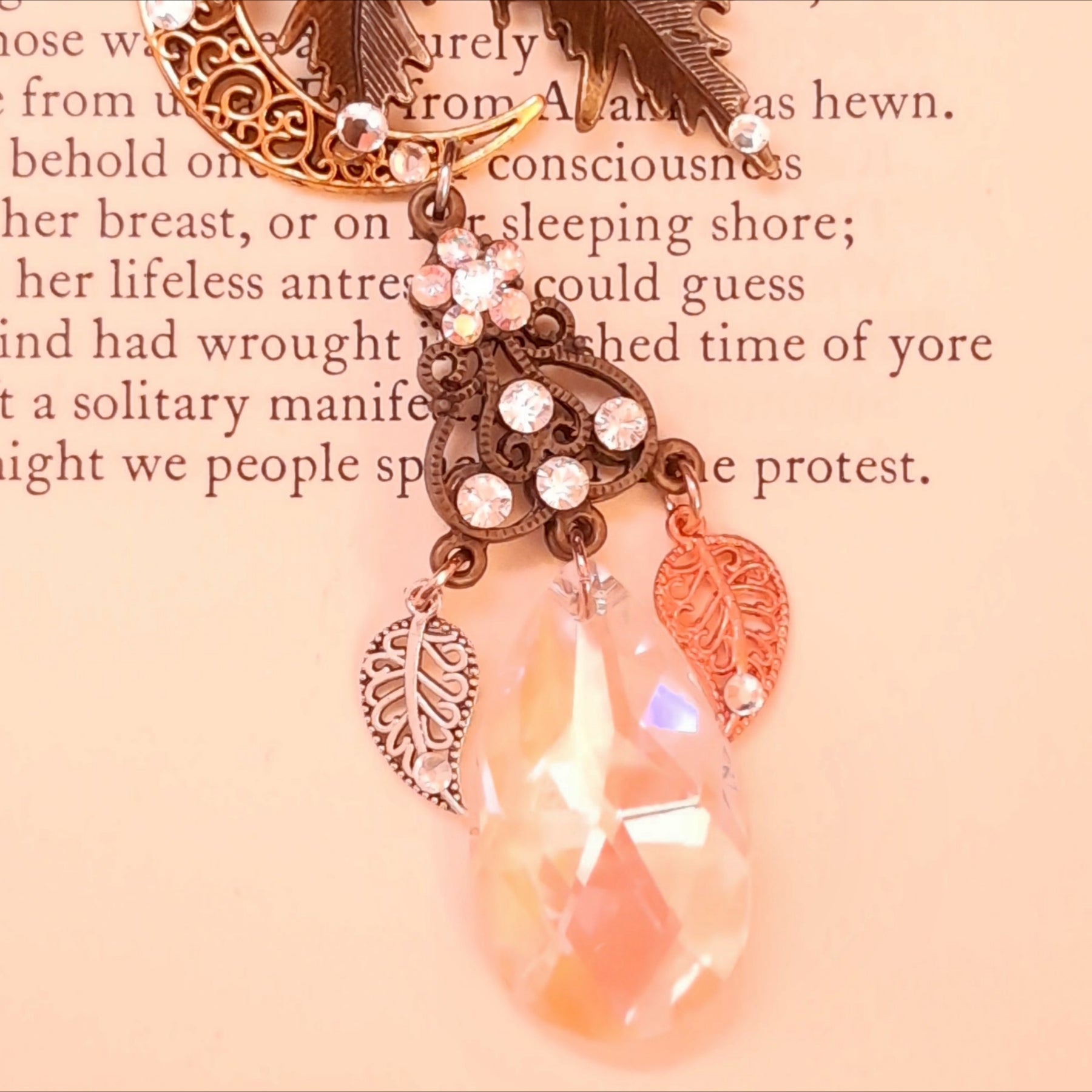 Rachel Flam Design Victorian style and vintage style fantasy necklace detail on a book page, showing a Swarovski® crystal flower, decorated openwork connector, leaf charms, and iridescent teardrop.
