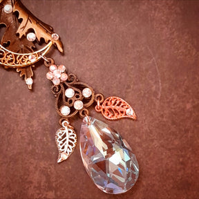 Close view of a faceted Swarovski® crystal teardrop between two openwork leaf charms on a Rachel Flam Design Victorian style and vintage style fantasy necklace, with a crystal flower above.