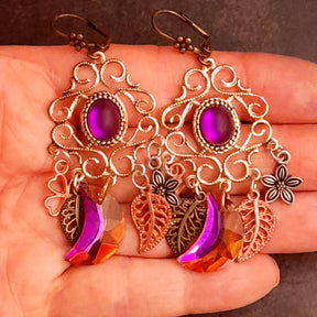 Fuchsia Swarovski crescent earrings shown in hand with ornate scrollwork, flowers, and leaves in Victorian style and vintage style by Rachel Flam Design