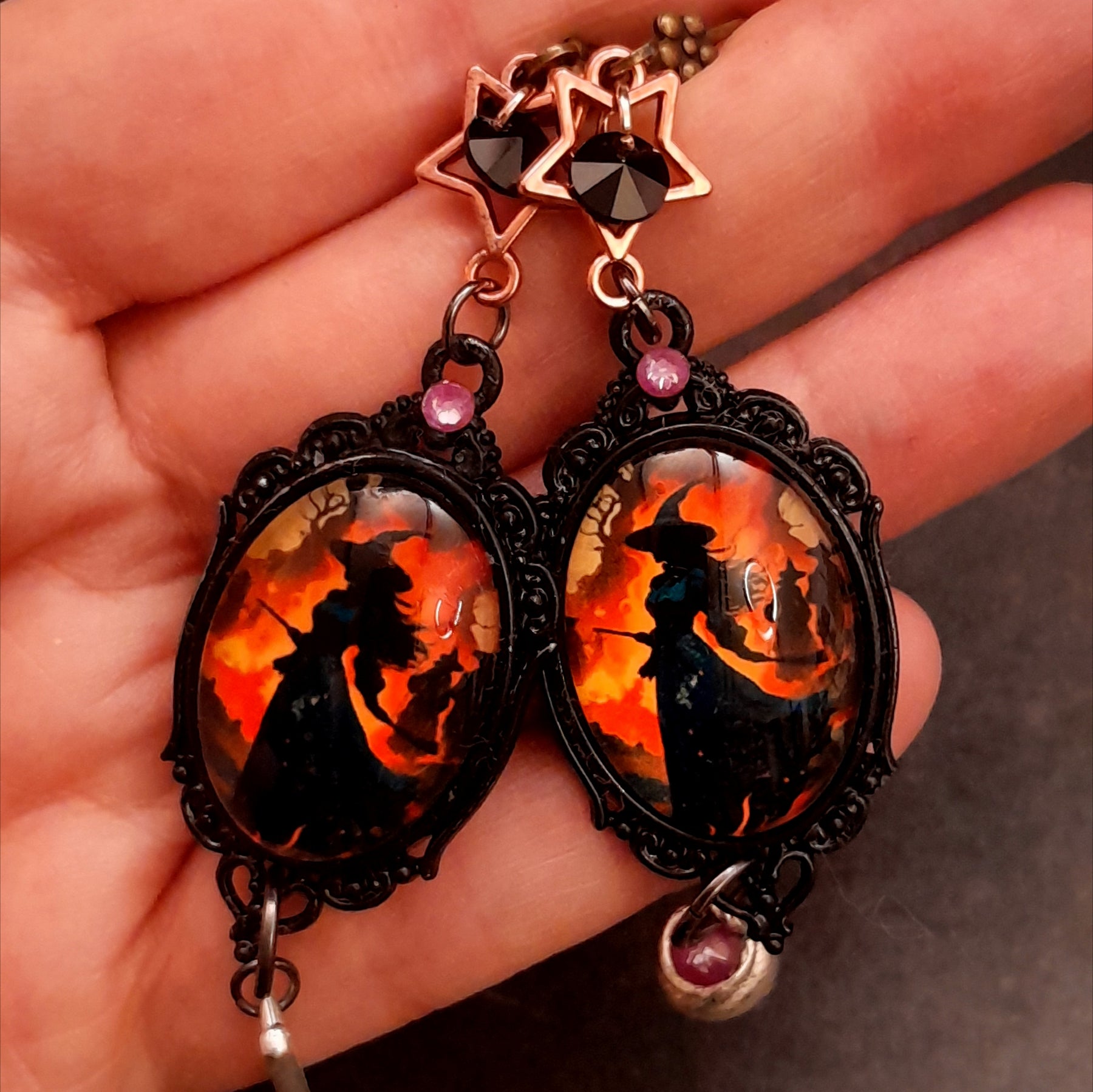 Halloween handmade witch portrait earrings held in hand with star accents, black and purple Swarovski crystals, ornate frames and mismatched charms in Victorian style and vintage style by Rachel Flam Design