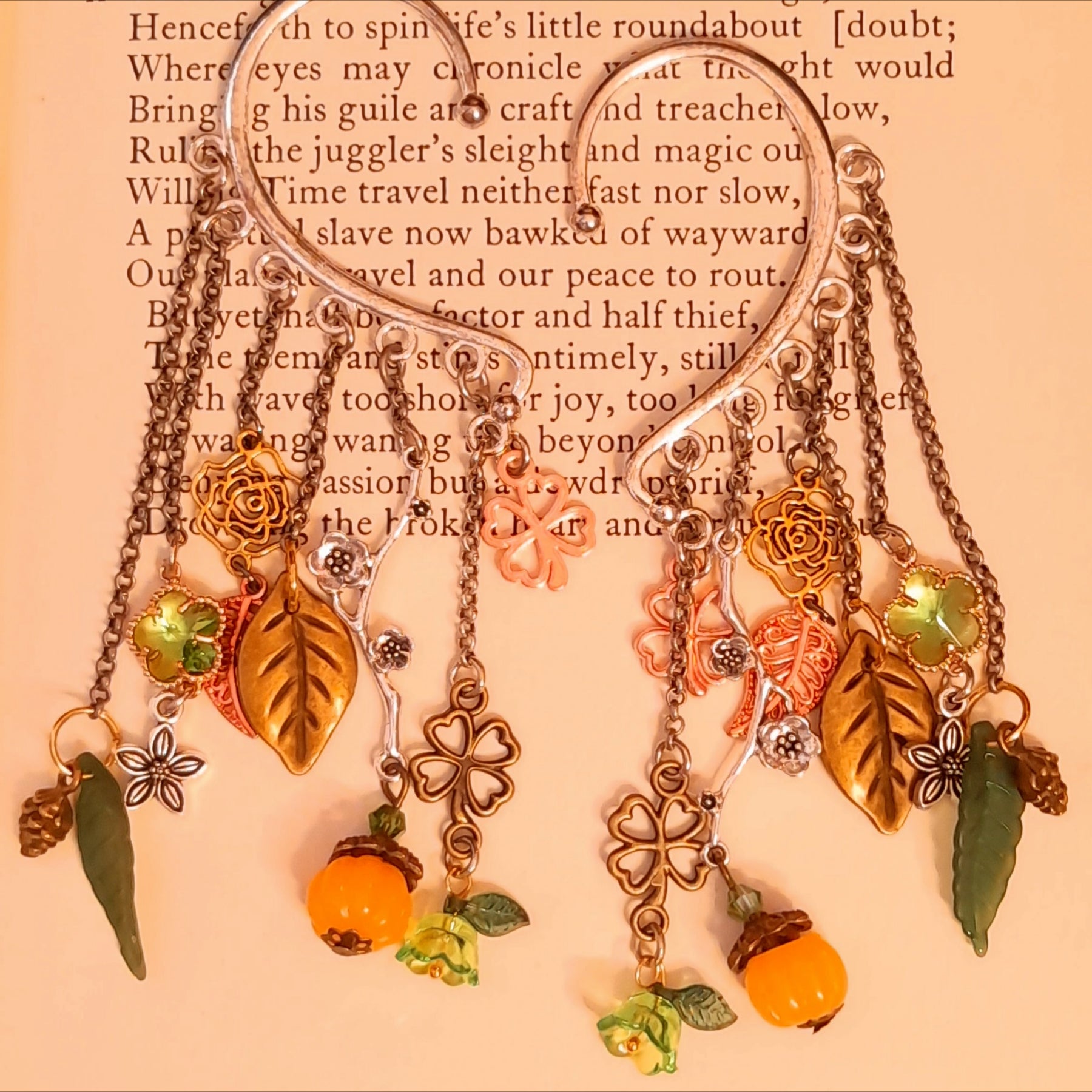 Victorian style and vintage style floral ear wrap cuffs by Rachel Flam Design, featuring green Swarovski crystals, pumpkin drops and woodland charms displayed on an open book.