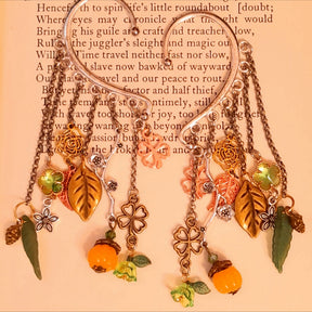 Victorian style and vintage style floral ear wrap cuffs by Rachel Flam Design, featuring green Swarovski crystals, pumpkin drops and woodland charms displayed on an open book.