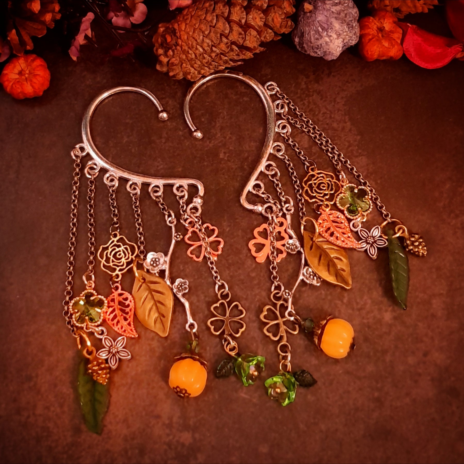 Victorian style and vintage style non pierced ear wrap cuffs by Rachel Flam Design, with green Swarovski crystals, orange pumpkins, flowers and dangling leaves on a dark background.