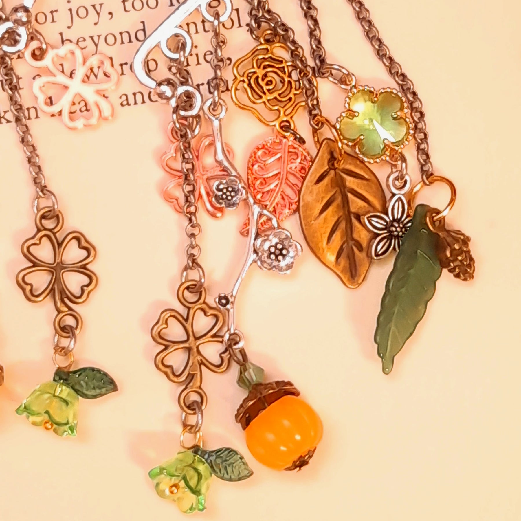 Victorian style and vintage style woodland ear wrap detail by Rachel Flam Design, showing green Swarovski crystals, a long green leaf, pinecone charm and orange pumpkin on an open book.