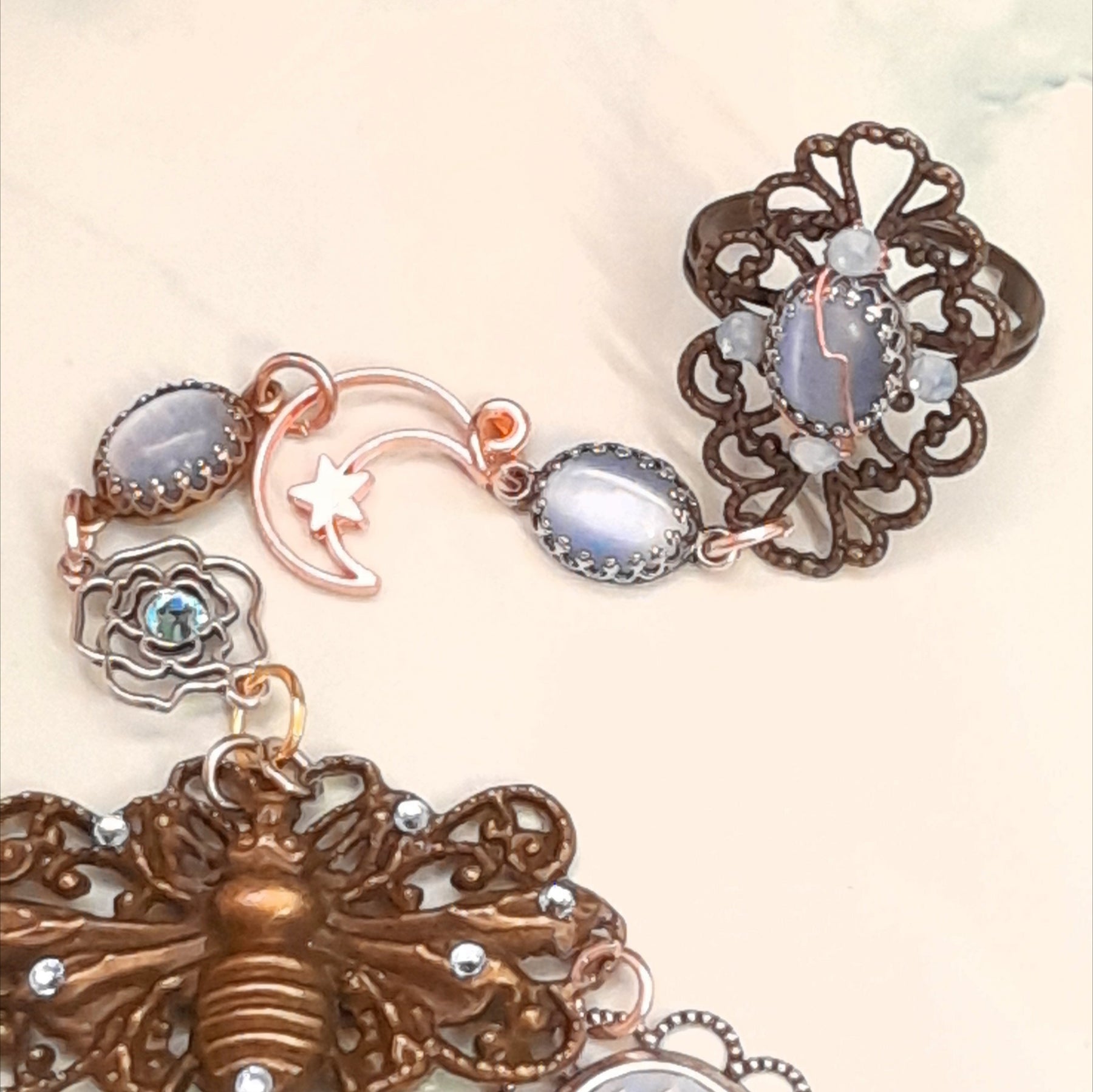 Magical fantasy bee hand chain slave bracelet  on wrist close up of bracelet portion showing blue floral cameo open rose charm and rose bud charms with blue Swarovski crystals Victorian style vintage style