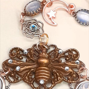 Handmade fantasy bee hand chain slave bracelet  flat lay close up of dramatic bee centerpiece filigree backing crescent moon charm and open rose charm with blue Swarovski crystals Victorian style vintage style