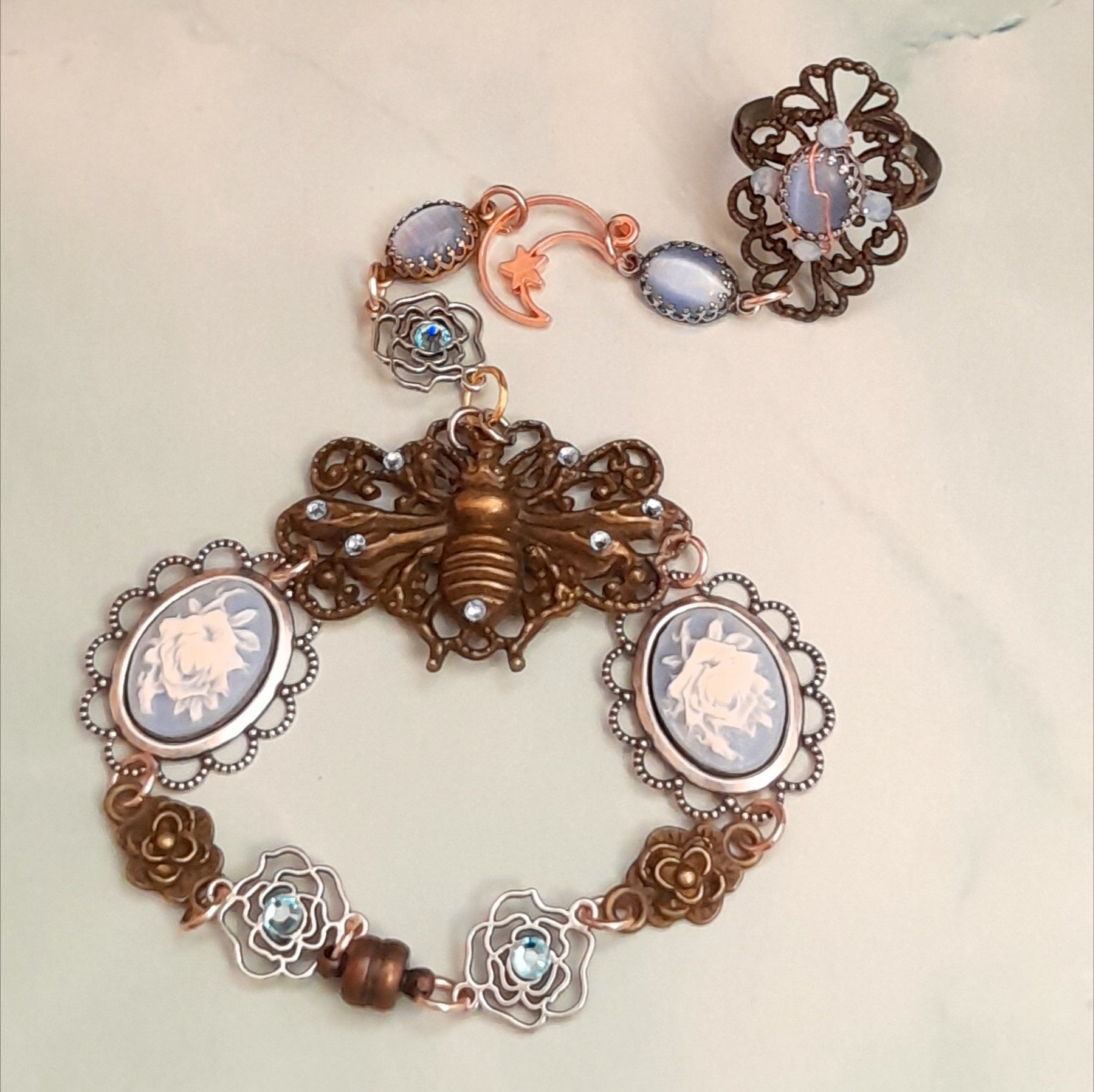 Magical fantasy bee hand chain slave bracelet worn on hand top down view showing full piece from filigree ring to bee centerpiece with blue Swarovski crystals Victorian style vintage style