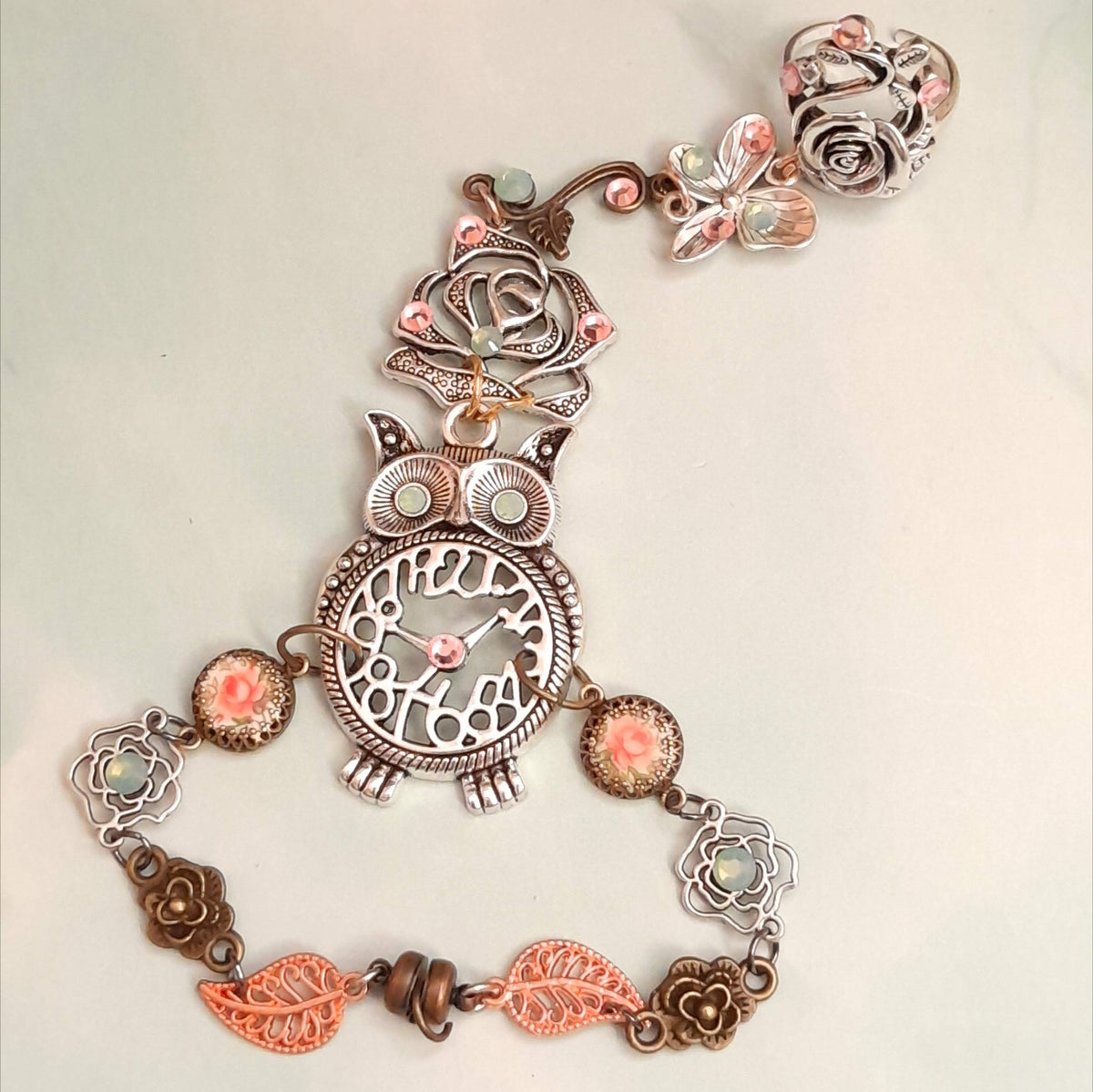 Magical fantasy owl hand chain flat lay showing full piece with rose ring butterfly charm owl centerpiece pink rose cameos and leaf links with Swarovski crystals Victorian style vintage style