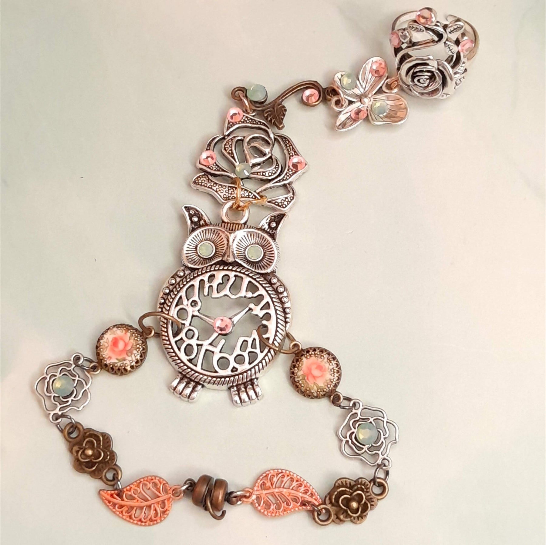 Magical fantasy owl hand chain flat lay showing full piece with rose ring butterfly charm owl centerpiece pink rose cameos and leaf links with Swarovski crystals Victorian style vintage style