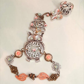 Magical fantasy owl hand chain flat lay showing full piece with rose ring butterfly charm owl centerpiece pink rose cameos and leaf links with Swarovski crystals Victorian style vintage style