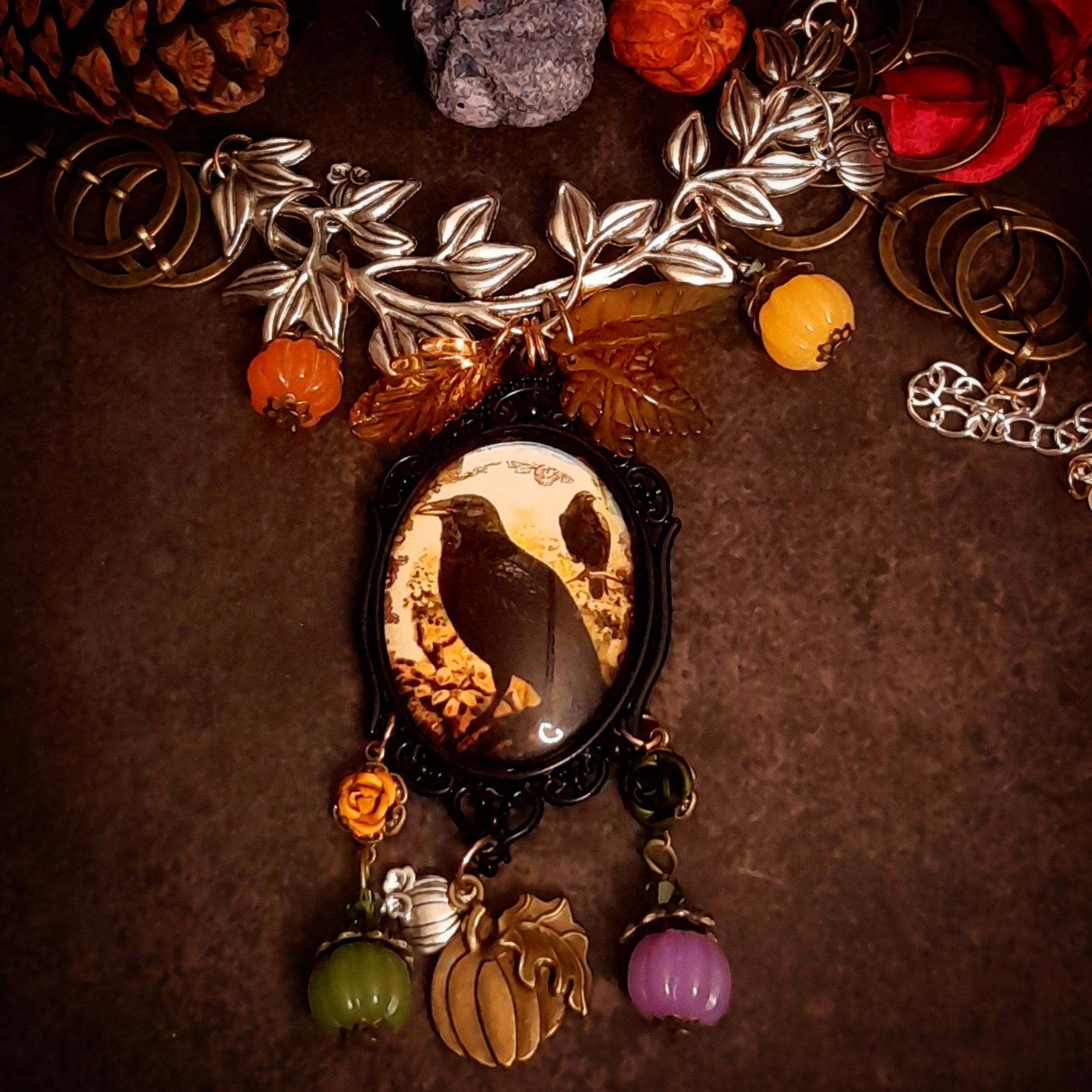 Full view of handmade black crow and pumpkin necklace with leafy branches, raven artwork, roses, green and purple pumpkins, crystal accents, and dangling autumn details, Victorian style and vintage style fantasy jewelry by Rachel Flam Design