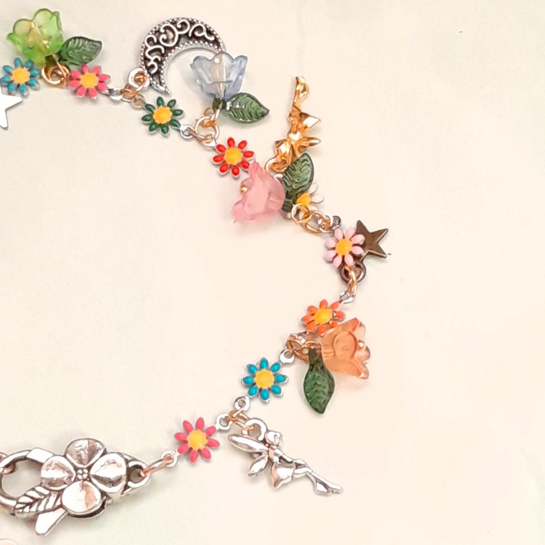 Handmade celestial fairy anklet worn on ankle showing crescent moon charm, star charm, multicolor enamel daisy flowers, orange and red flower beads, and leaf charms, Victorian style vintage style