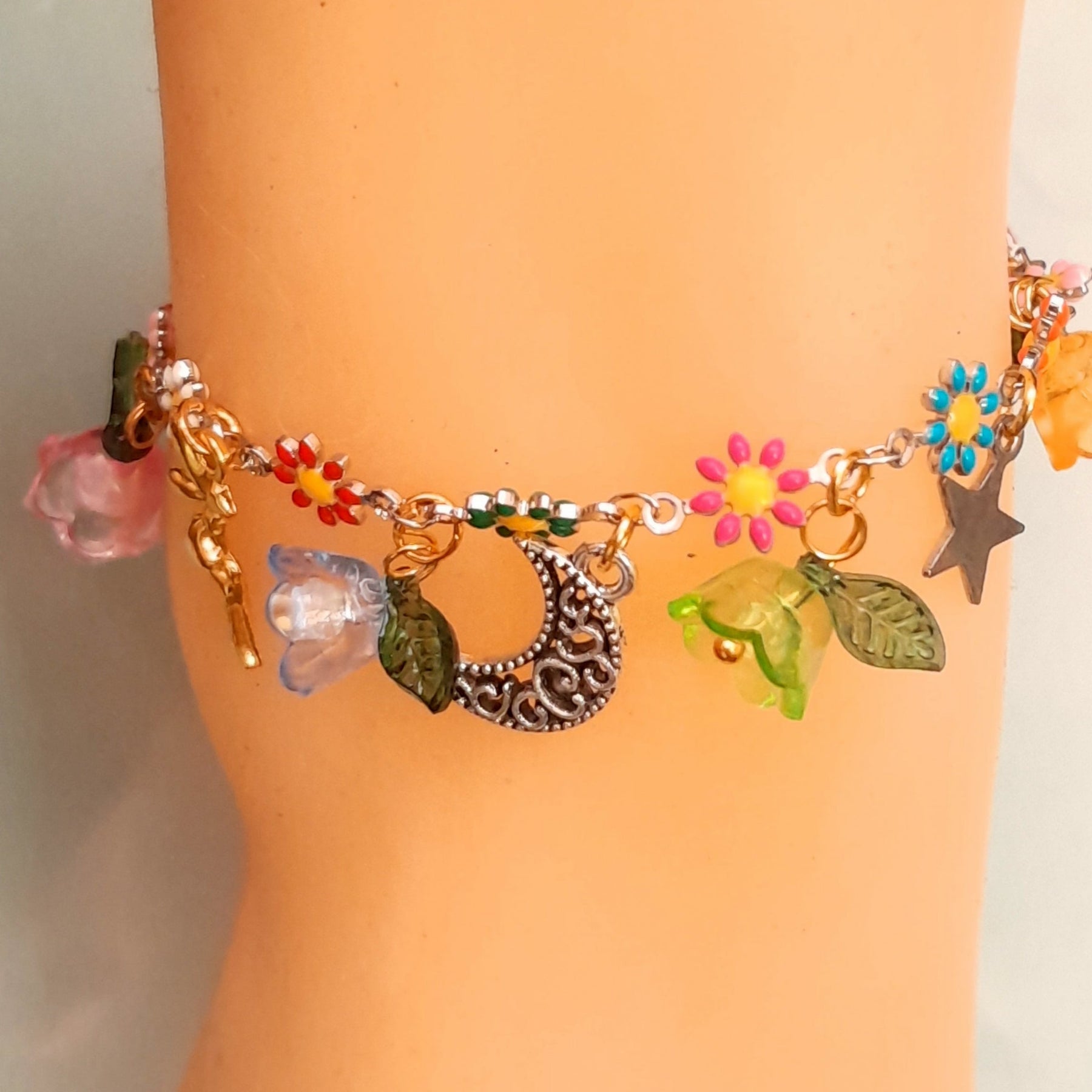 Handmade celestial fairy charm anklet featuring fairy figures, ornate crescent moon, star charms, multicolor enamel daisy flowers, and colorful flower beads with leaf accents, Victorian style vintage style