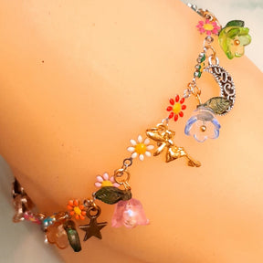 Handmade fairy moon charm anklet worn on ankle with fairy figure, enamel daisy flowers, red flower bead, leaf charm, crescent moon, and lobster clasp detail, Victorian style vintage style fantasy jewelry