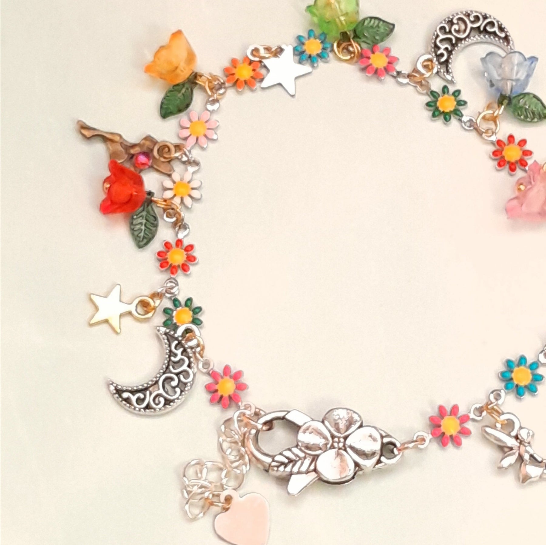 Closeup of handmade fantasy fairy anklet showing ornate crescent moon charm, star charm, fairy figure, multicolor enamel daisy flowers, pink and orange flower beads, and leaf charms, Victorian style vintage style