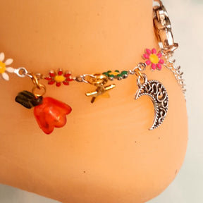 Handmade fantasy fairy moon charm anklet worn on ankle with fairy figure, crescent moon, star charm, multicolor enamel daisy flowers, pink and blue flower beads, and leaf charms, Victorian style vintage style