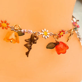 Handmade rainbow fairy charm anklet worn on ankle with crescent moon, star charm, multicolor enamel daisy flowers, green and orange flower beads, and leaf charms, styled with roses, Victorian style vintage style
