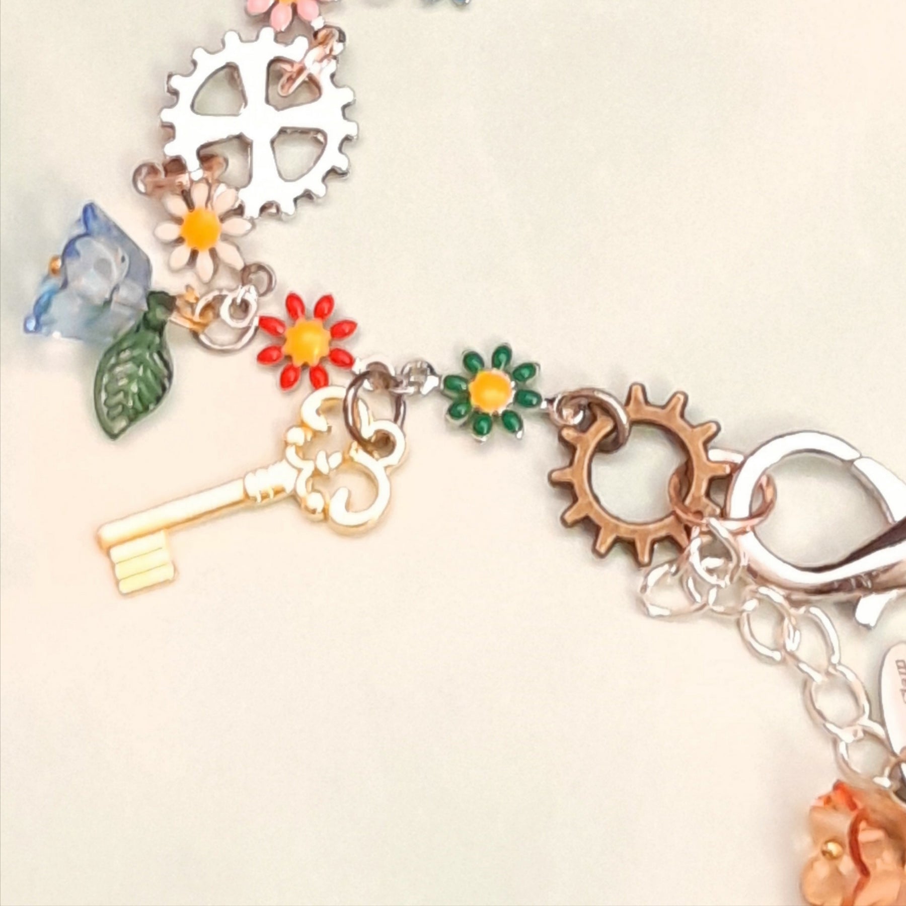 Full view of handmade rainbow steampunk charm anklet with multiple vintage keys, gear and cog charms, multicolor enamel daisy flowers, and crystal beads, Victorian style vintage style